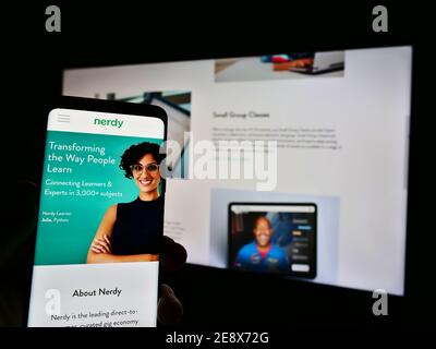 Person holding mobile phone with company website and logo of US e-learning platform provider Nerdy Inc on display. Focus on center of phone screen. Stock Photo