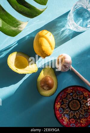 Ingredients for fresh Mexican Guacamole, two Avocado halves, garlic and lime/ lemon isolated on turquoise blue background Stock Photo
