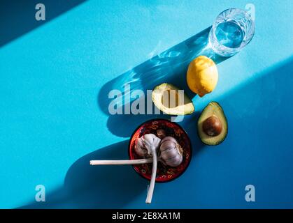 Ingredients for fresh Mexican Guacamole, two Avocado halves, garlic and lime/ lemon isolated on turquoise blue background Stock Photo