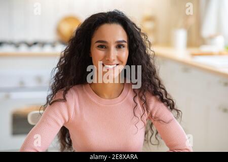Portraif of happy young brunette woman sitting at table in kitchen Stock Photo
