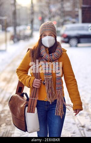 Middle-aged brunette woman in winter clothes wearing face mask outdoors due to Corona virus outdoors while on her way to work Stock Photo