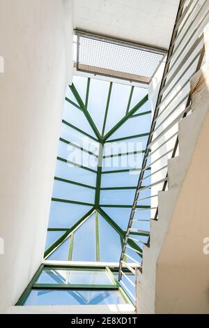 Top of concrete stair case with white walls and green hand rail in modern clean multi storey carpark looking up to skylight on bright sunny day Stock Photo