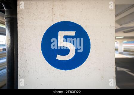 White coloured hand painted level number five in the middle of a blue colour circle painted on an old textured concrete pillar wall Stock Photo