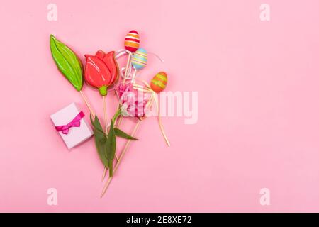 Spring greeting card concept. A bouquet of tulips, cookies in the form of a tulip, Easter eggs and a small box with a spice lies on a pink background. Stock Photo