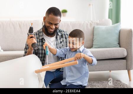 African Boy Helping Father Fix Table Doing Housework At Home Stock Photo