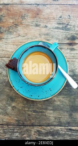 Top down photograph of an espresso cup in a green turquoise espresso cup with a chocolate brownie and a spoon on a rustic wooden table