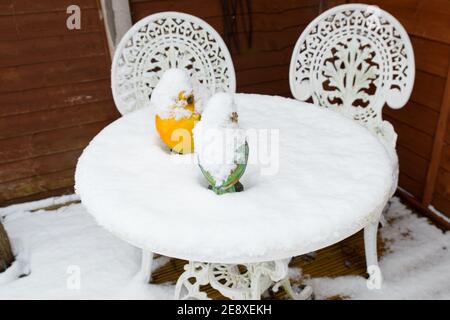 close up of patio table and chairs covered in snow on decking.  bird ornaments on table are covered in snow Stock Photo