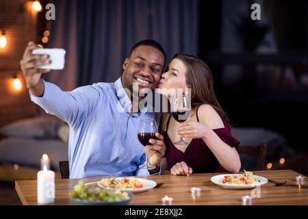 Multiracial couple in love taking selfie while having romantic dinner at restaurant Stock Photo