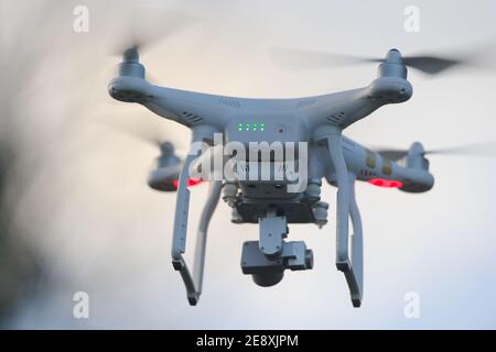 Great Malvern, United Kingdom, 27th December, 2020: Rear view of a white quadcopter drone with lights, against blue evening sky. Motion blur propeller Stock Photo