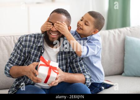 Little Son Congratulating Black Father Giving Wrapped Gift Indoors Stock Photo
