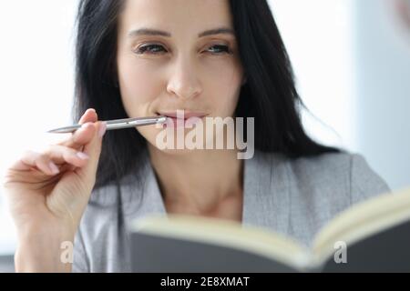 Portrait of young brunette woman with ballpoint pen in her mouth Stock Photo