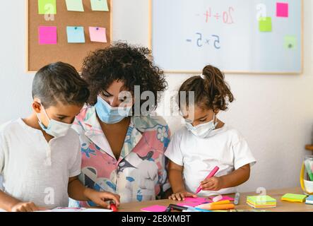 Teacher with children wearing face mask in preschool classroom during corona virus pandemic - Healthcare and education concept Stock Photo