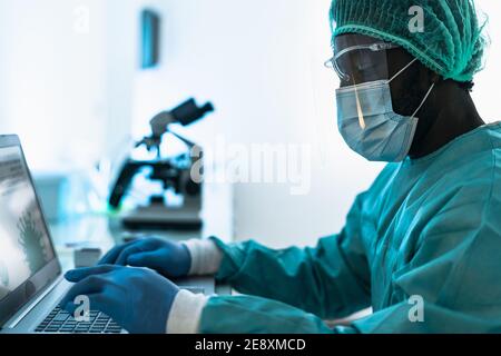 Medical worker wearing personal protective equipment using computer inside clinic during corona virus outbreak - Research and development concept Stock Photo