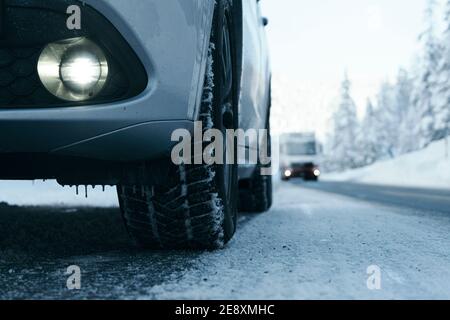 Close-up of winter car tires with alloy wheel and bumper of sport utility vehicle on icy mountain road covered with snow, Italy Stock Photo