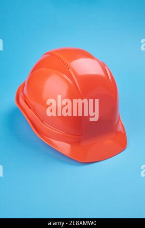 orange protective helmet and safety glasses near it on a bright blue background. protective workwear and construction industry concept Stock Photo