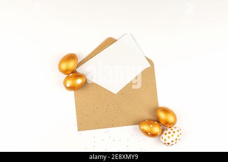 Easter festive decoration. Top view of easter eggs colored with golden paint and empty mock-up card in a kraft envelope. Various dotted designs. White Stock Photo
