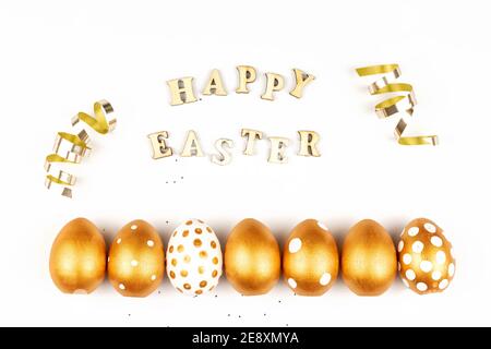 Easter festive decoration. Top view of easter eggs colored with golden paint and inscription in English Happy Easter. Wooden letters on white backgrou Stock Photo