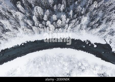 Overhead view of frozen river crossing a winter forest covered with snow, Switzerland Stock Photo