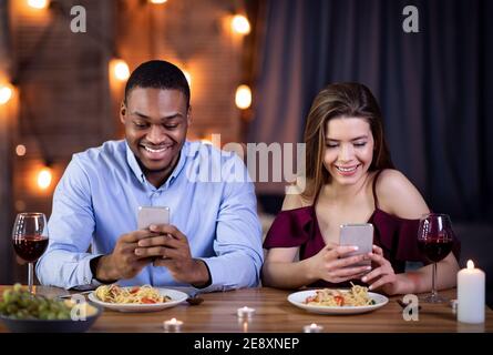 Phubbing. Young Interracial Couple Looking At Their Smartphones At Date In Restaurant Stock Photo