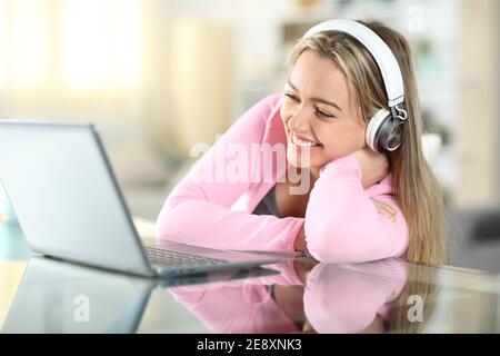 Happy teen with headphones watching media on laptop smiling at home Stock Photo