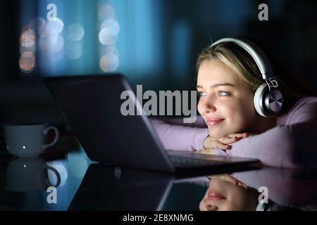 Satisfied teen wearing headphones watching media on laptop in the night at home Stock Photo