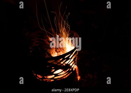 Long exposure photograph of a camp pit fire with a piece of wood on it in the dark at nighttime with dark background Stock Photo