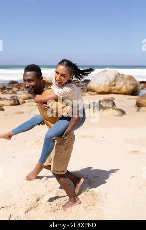 African american couple piggybacking on a beach by the sea Stock Photo