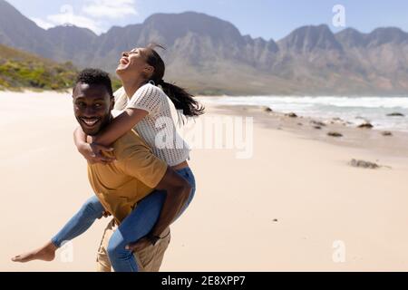 African american couple having fun piggybacking on a beach by the sea Stock Photo