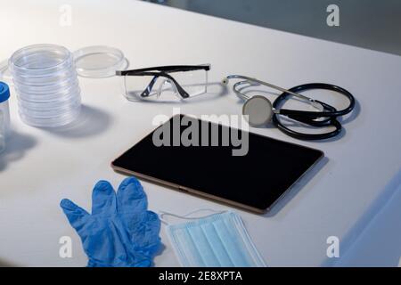 Desk in doctors surgery with tablet computer face mask gloves and stethoscope Stock Photo