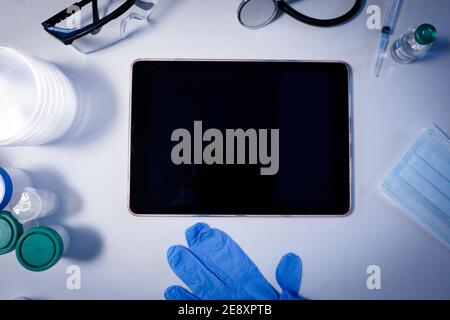 Desk in doctors surgery with tablet computer face mask gloves and stethoscope Stock Photo