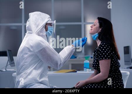 Caucasian male medical worker wearing protective clothing taking swab of masked female patient Stock Photo