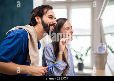 Young couple brushing teeth in front of mirror indoors at home. Stock Photo