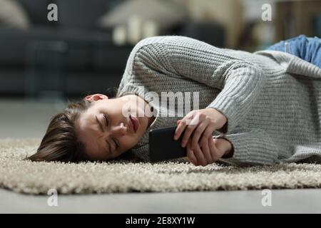 Sad teen reading bad news on smart phone lying on the floor at home Stock Photo