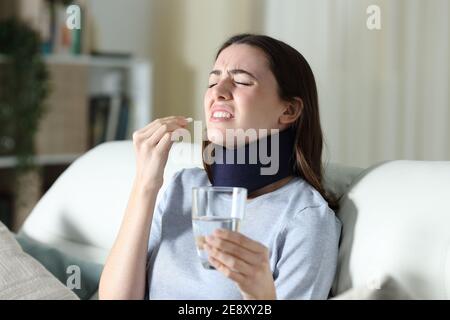 Disabled woman wearing neck brace suffering ache taking pill at home Stock Photo