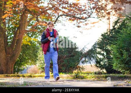 Woman caregiver, nurse or healthcare worker outdoors on the way to work, using smartphone. Stock Photo