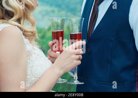 Glasses with red champagne drink in bride and groom hands. Happy newlyweds drinking. Loving couple created new family. Stock Photo