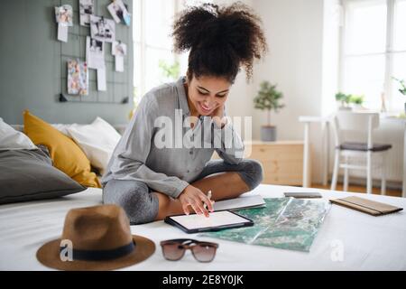 Young woman with tablet and map indoors at home, planning traveling trip. Stock Photo