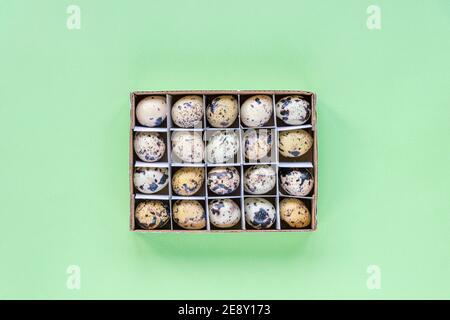 Quail eggs in a cardboard box on a green background. Easter concept. Top view, flat lay, copy space. Stock Photo