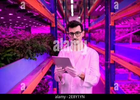 Worker with tablet on aquaponic farm, sustainable business and artificial lighting. Stock Photo