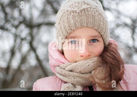 Sad child girl in warm knitted winter clothes spent time outdoors and got frozen. Stock Photo