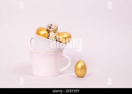 Easter composition of golden decorative and quail eggs in porcelain cups on a pink background. Selective focus, copy space. Stock Photo