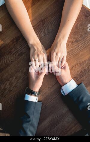 Loving couple siting at the round wooden table, gently holding hands. High angle view Stock Photo