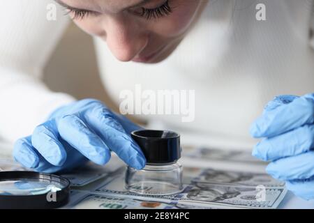 Woman in rubber gloves looking at dollar bills through magnifying glass Stock Photo