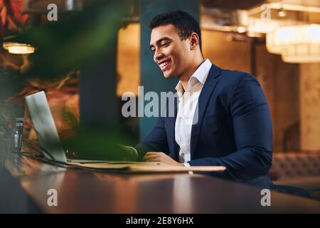 Joyful dark-haired male teleworker using his laptop Stock Photo