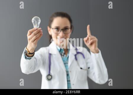 Woman doctor holding light bulb in hands and showing index finger up Stock Photo