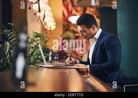 Concentrated dark-haired entrepreneur jotting down his ideas Stock Photo