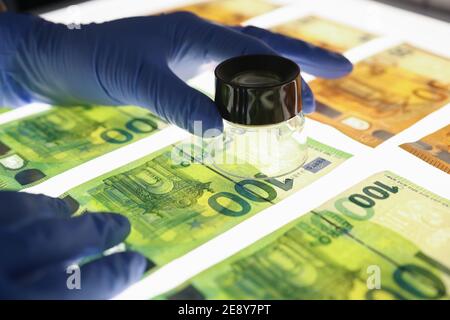 Hands in rubber gloves holding magnifying glass with banknotes closeup Stock Photo