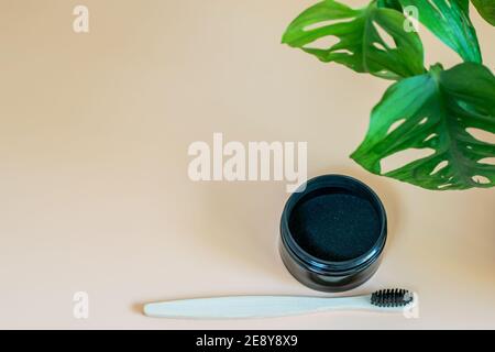 Activated organic charcoal and bamboo toothbrush for teeth whitening on neutral beige background, monstera leaf as decorative natural element. Healthy Stock Photo