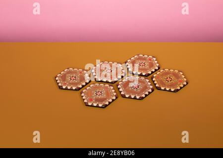 Vintage marquetery coasters with brown and beige colors. An eclectic oriental pattern made from mosaic wood on an ochre table and a pink background Stock Photo