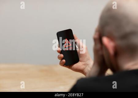 A malware text and warning sign popping up on a cell phone screen. A desperate man holding his hacked infected phone. Stock Photo